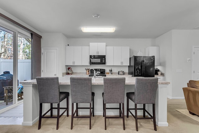 kitchen with a kitchen bar, black appliances, an island with sink, light stone countertops, and white cabinets