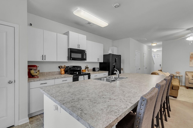 kitchen with sink, a breakfast bar area, white cabinets, black appliances, and a center island with sink