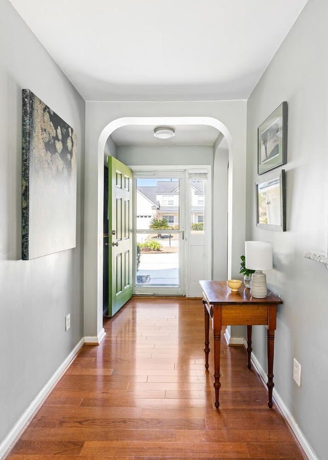 foyer featuring arched walkways, wood finished floors, and baseboards