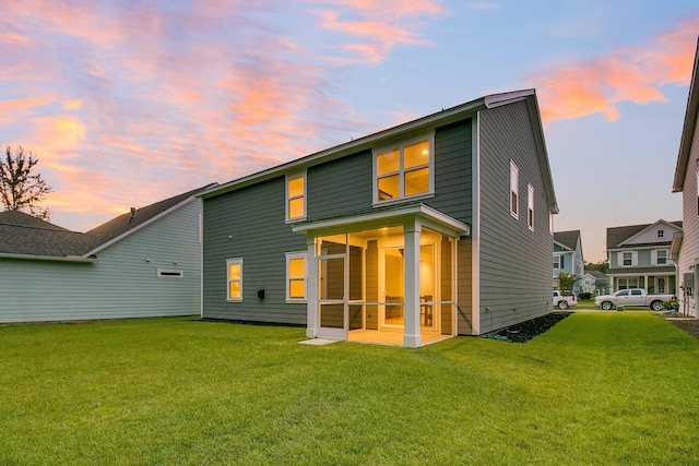 back house at dusk featuring a lawn