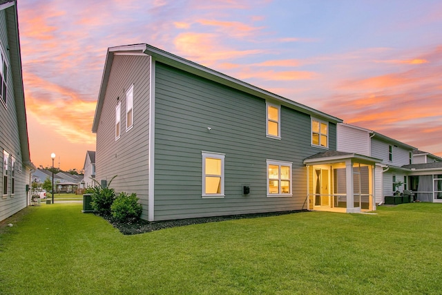 back house at dusk featuring a lawn and a sunroom