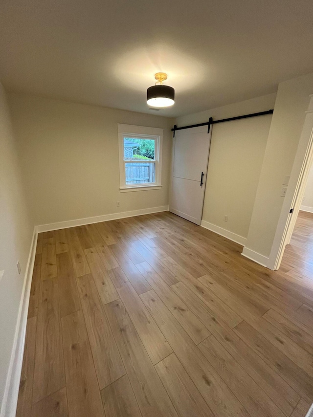 unfurnished bedroom with a barn door and light hardwood / wood-style flooring