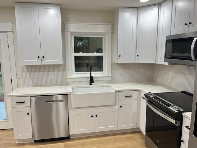 kitchen with light wood-type flooring, appliances with stainless steel finishes, a wealth of natural light, and white cabinetry