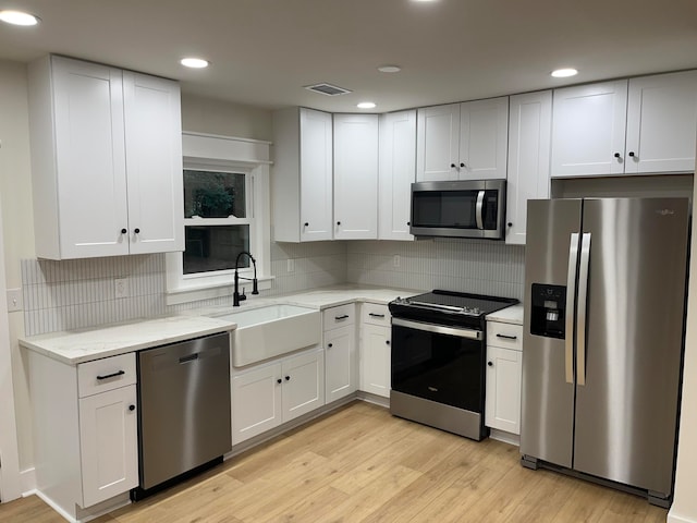 kitchen with appliances with stainless steel finishes, white cabinetry, and light hardwood / wood-style floors