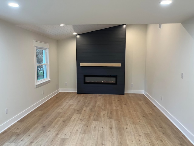 unfurnished living room featuring a large fireplace, light hardwood / wood-style floors, and vaulted ceiling