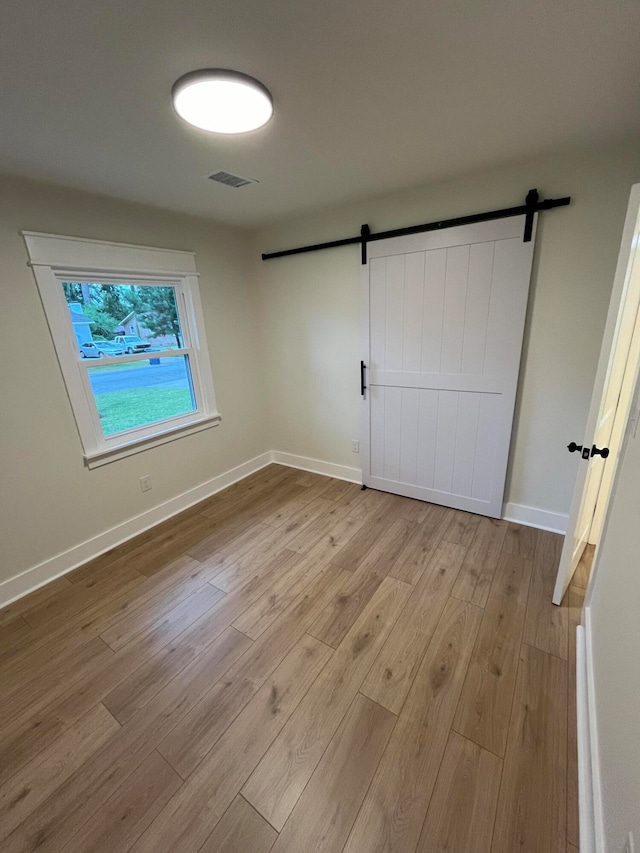 unfurnished bedroom featuring a barn door and light hardwood / wood-style floors