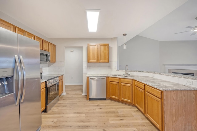 kitchen with decorative light fixtures, stainless steel appliances, light wood-style floors, a sink, and a peninsula