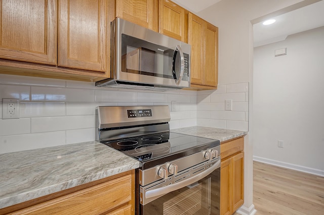 kitchen featuring baseboards, appliances with stainless steel finishes, backsplash, light stone countertops, and light wood finished floors