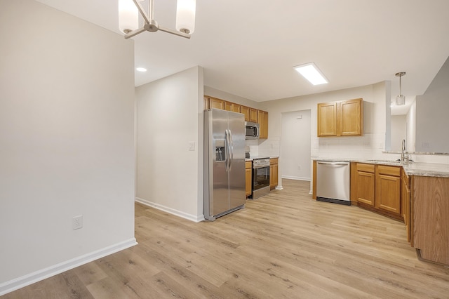 kitchen with a sink, appliances with stainless steel finishes, backsplash, light wood finished floors, and pendant lighting