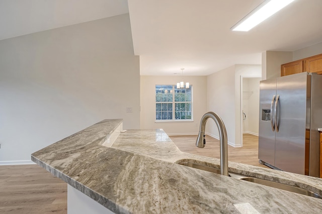 kitchen featuring light wood-type flooring, a sink, hanging light fixtures, and stainless steel fridge with ice dispenser