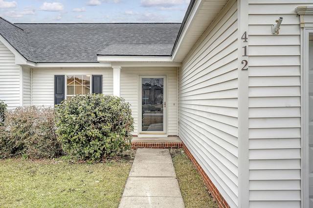 view of exterior entry with a yard and roof with shingles