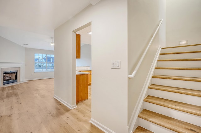 staircase featuring a fireplace with flush hearth, a ceiling fan, wood finished floors, visible vents, and baseboards