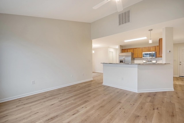 kitchen with stainless steel appliances, a peninsula, visible vents, light wood-type flooring, and light stone countertops