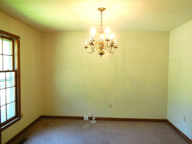 carpeted empty room featuring an inviting chandelier and a textured ceiling