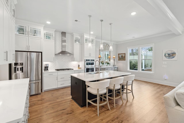 kitchen with white cabinetry, stainless steel appliances, a kitchen island with sink, and wall chimney range hood