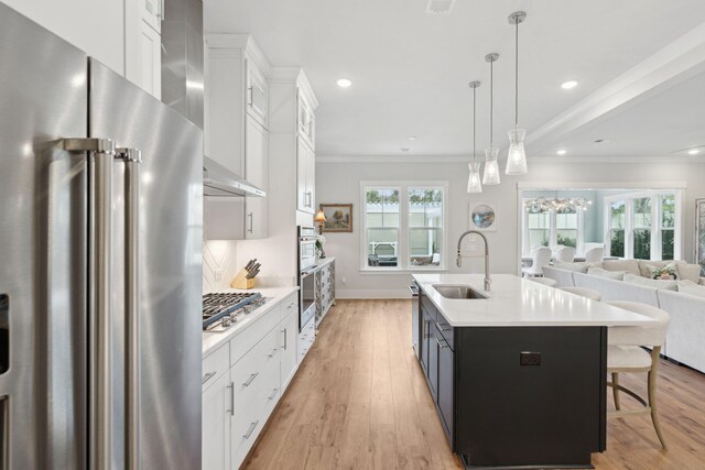 kitchen with pendant lighting, an island with sink, sink, white cabinets, and stainless steel appliances