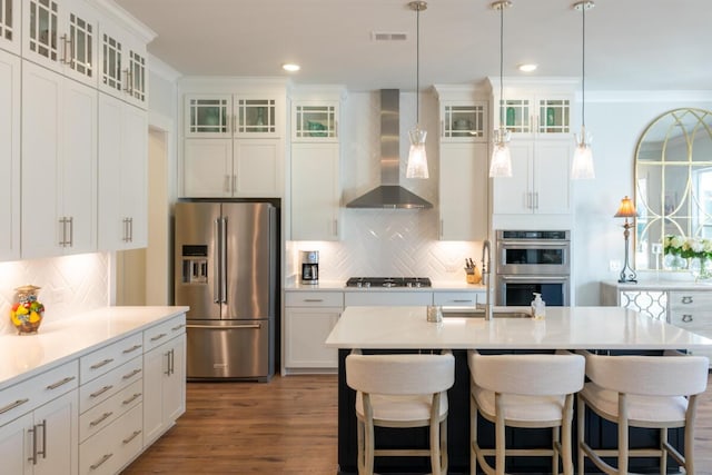 kitchen featuring white cabinets, stainless steel appliances, an island with sink, and wall chimney exhaust hood