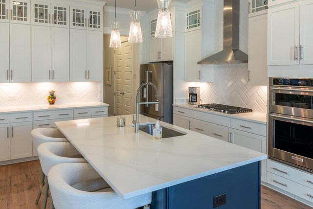 kitchen with a center island with sink, appliances with stainless steel finishes, a breakfast bar area, and wall chimney range hood