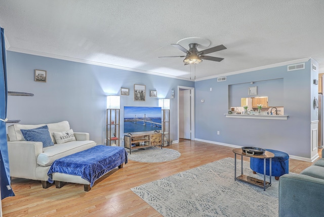 living room featuring a textured ceiling, visible vents, wood finished floors, ceiling fan, and crown molding