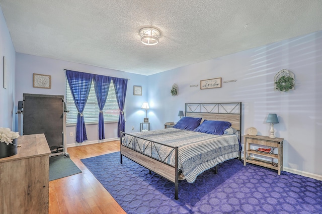 bedroom with wood finished floors, a textured ceiling, and baseboards