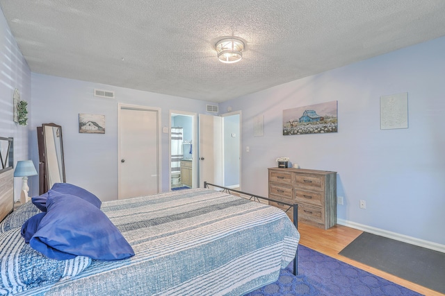 bedroom featuring visible vents, baseboards, wood finished floors, and a textured ceiling
