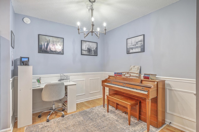 home office with a decorative wall, a textured ceiling, light wood-type flooring, a wainscoted wall, and a notable chandelier