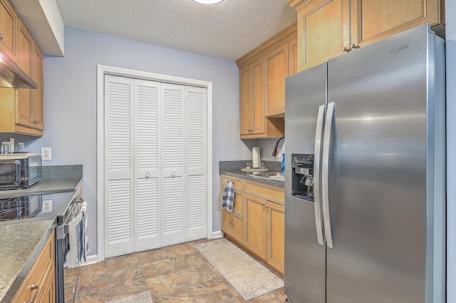 kitchen featuring stainless steel appliances, dark countertops, a sink, stone finish flooring, and baseboards