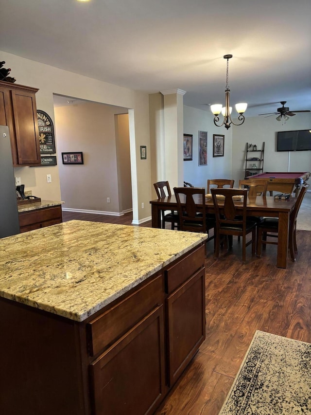 kitchen featuring dark wood-type flooring, hanging light fixtures, dark brown cabinets, light stone countertops, and ceiling fan with notable chandelier