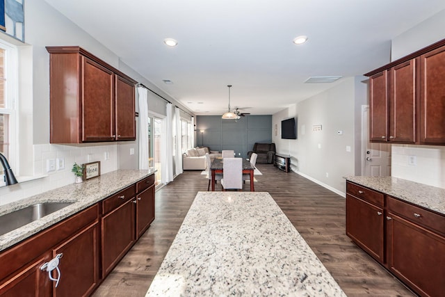 kitchen with dark wood-type flooring, ceiling fan, light stone counters, and sink