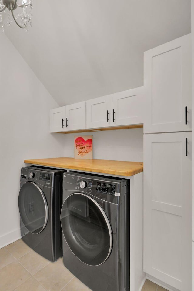 clothes washing area with a chandelier, washer and clothes dryer, light tile patterned floors, and cabinets