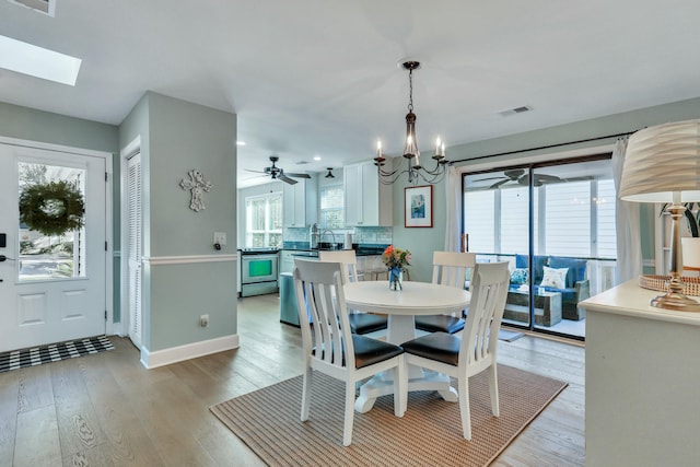 dining room with ceiling fan with notable chandelier, light hardwood / wood-style floors, a skylight, and sink