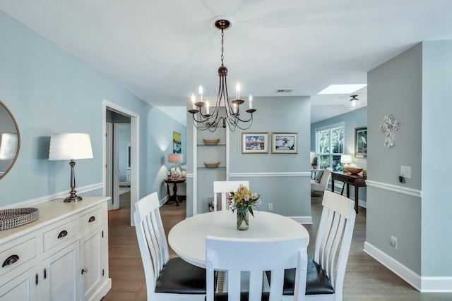 dining space with hardwood / wood-style flooring, ceiling fan with notable chandelier, and a skylight