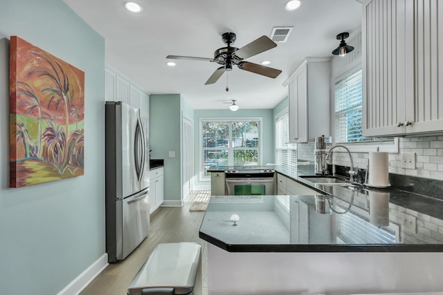 kitchen with sink, stainless steel appliances, kitchen peninsula, decorative backsplash, and light wood-type flooring