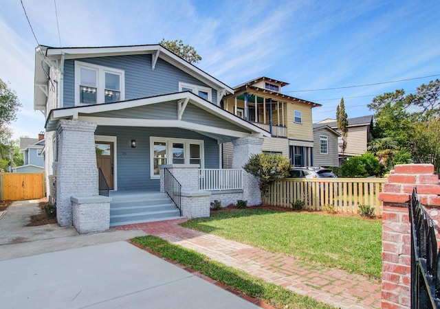 view of front of house featuring covered porch, brick siding, fence, and a front lawn