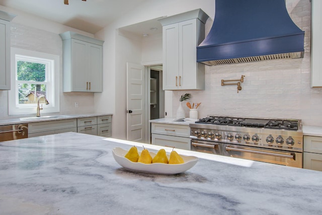 kitchen featuring custom exhaust hood, stainless steel appliances, backsplash, a sink, and light stone countertops