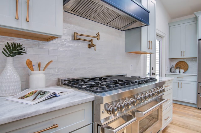 kitchen with range with two ovens, light wood finished floors, custom range hood, backsplash, and light stone countertops