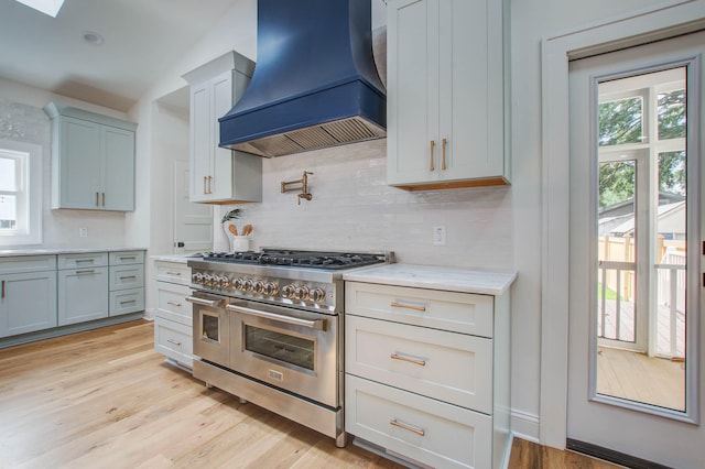 kitchen featuring a healthy amount of sunlight, light wood-type flooring, double oven range, and custom exhaust hood