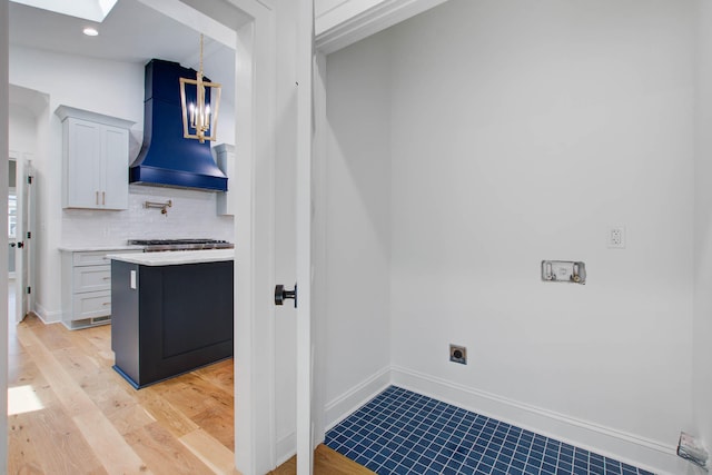 kitchen with a skylight, tasteful backsplash, decorative light fixtures, custom exhaust hood, and light countertops