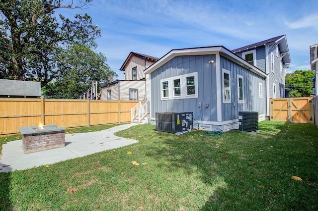 back of property with a fire pit, a patio, a fenced backyard, cooling unit, and board and batten siding