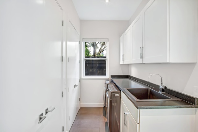 kitchen featuring sink, washer / dryer, light tile patterned flooring, and white cabinetry