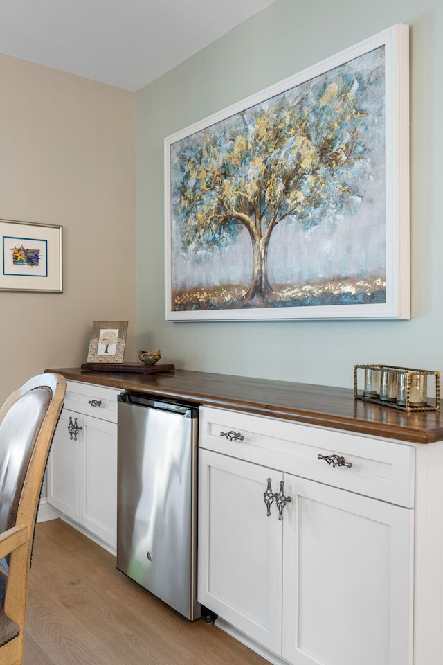 kitchen with stainless steel fridge, butcher block counters, light hardwood / wood-style floors, and white cabinetry