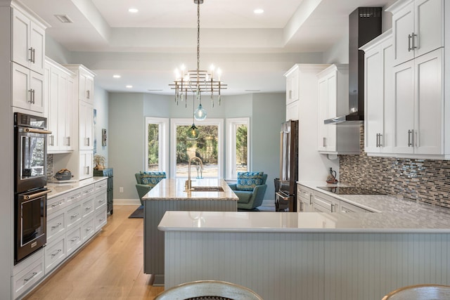 kitchen with light hardwood / wood-style floors, white cabinetry, hanging light fixtures, and a kitchen island with sink