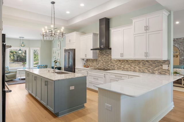 kitchen with pendant lighting, wall chimney exhaust hood, white cabinetry, and a kitchen island with sink