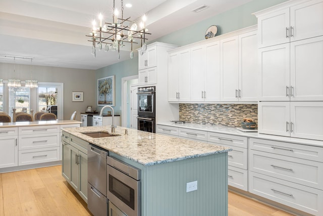 kitchen with white cabinets, appliances with stainless steel finishes, a kitchen island with sink, and pendant lighting