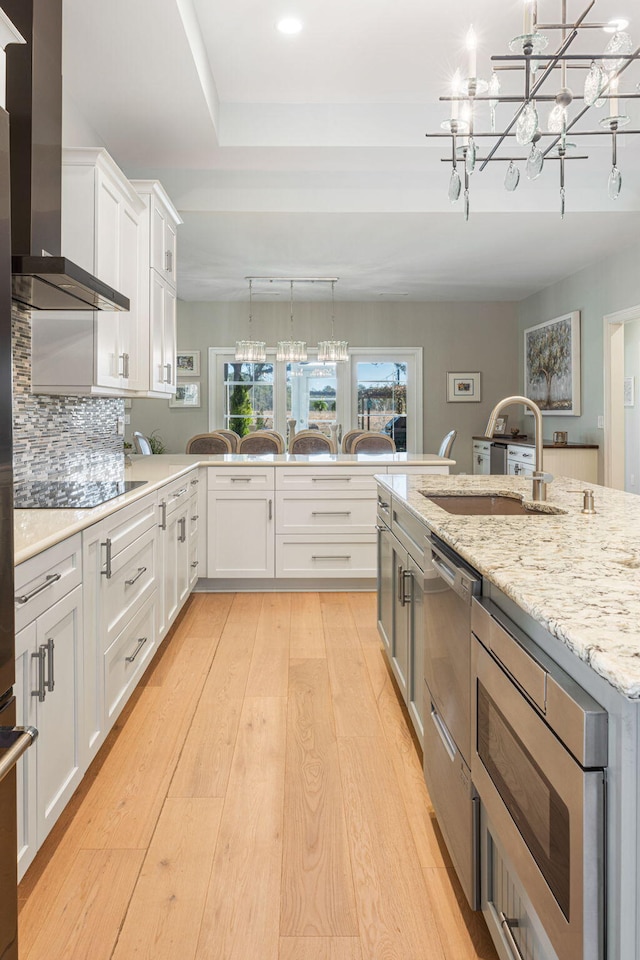 kitchen featuring pendant lighting, stainless steel microwave, white cabinetry, and wall chimney range hood