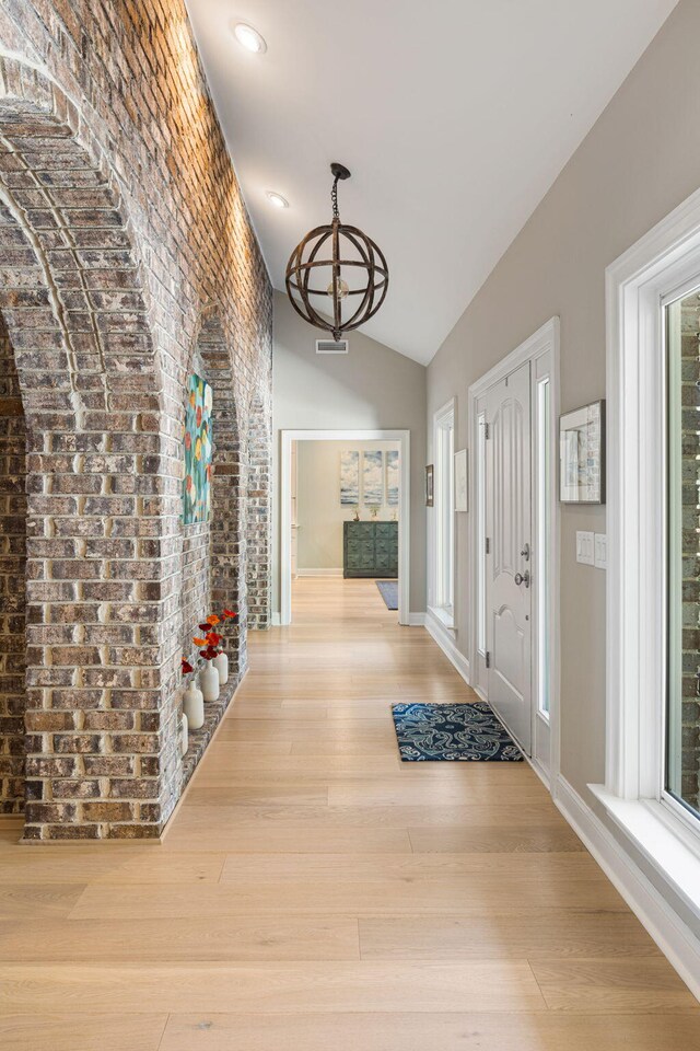 hallway with a chandelier, light wood-type flooring, plenty of natural light, and brick wall