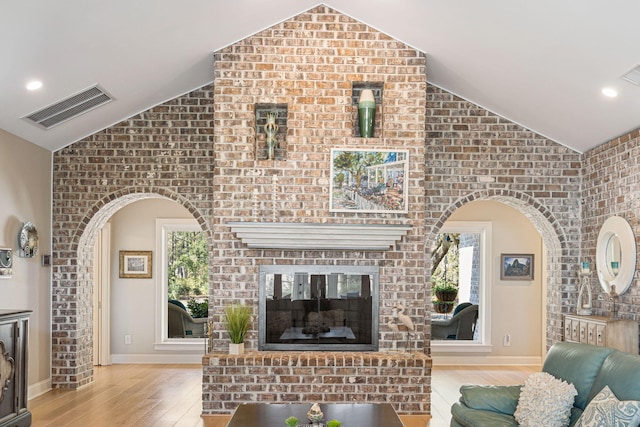 living room with light hardwood / wood-style floors, a brick fireplace, lofted ceiling, and brick wall