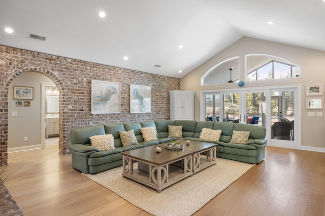 living room with light wood-type flooring, high vaulted ceiling, and brick wall