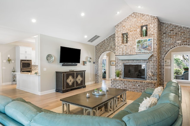 living room featuring lofted ceiling, light wood-type flooring, brick wall, and a brick fireplace