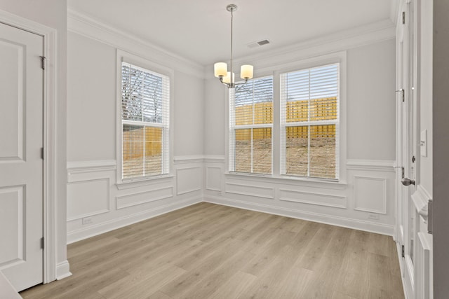unfurnished dining area featuring an inviting chandelier, light wood-style flooring, crown molding, visible vents, and wainscoting